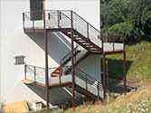 Utvändig trappa med stålstödstruktur, träplankor och glasräcken.