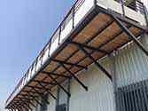 Balkong med stålstödstruktur, träplankor och glasräcken.